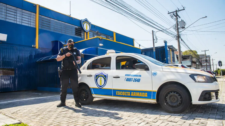 Vigilante uniformizado ao lado de veículo da Intersept identificado como escolta armada.
