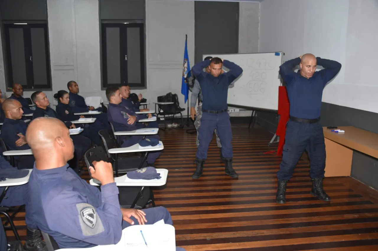 Instrutor fala durante atividade de formação, ao lado de um agente uniformizado da segurança pública.