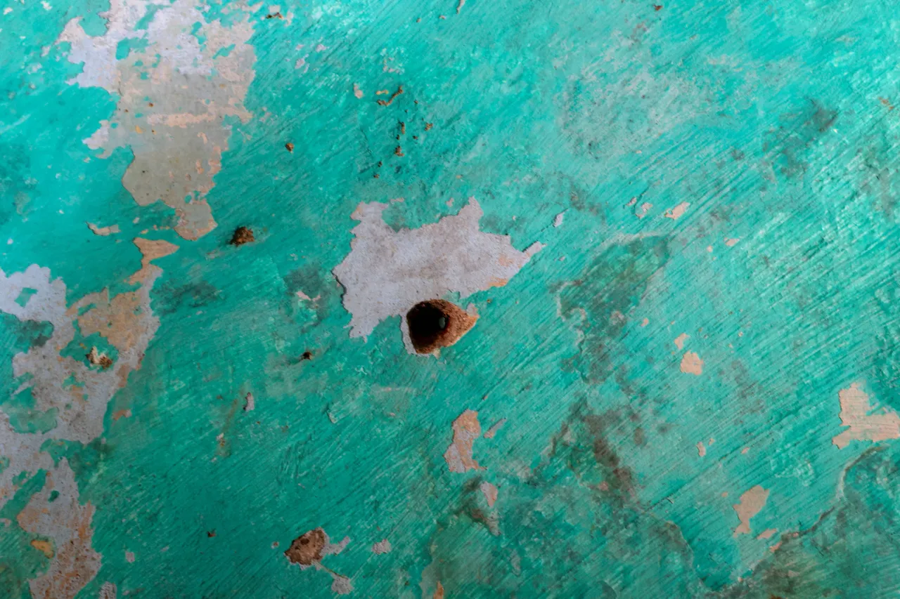 Parede interna verde descascada, com marcas de desgaste e um pequeno orifício escuro no centro.
